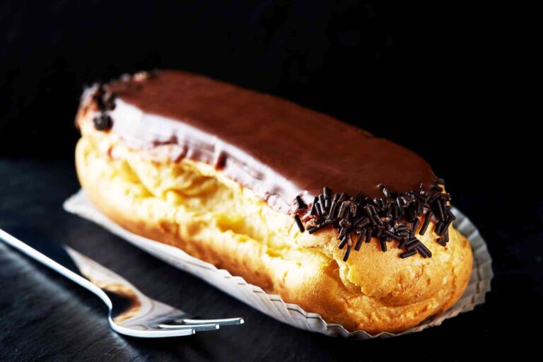 Single eclair with chocolate and a fork on a dark slate